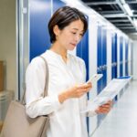 トランクルームの前でスマホと資料を見ながら料金やキャンペーンを確認する女性